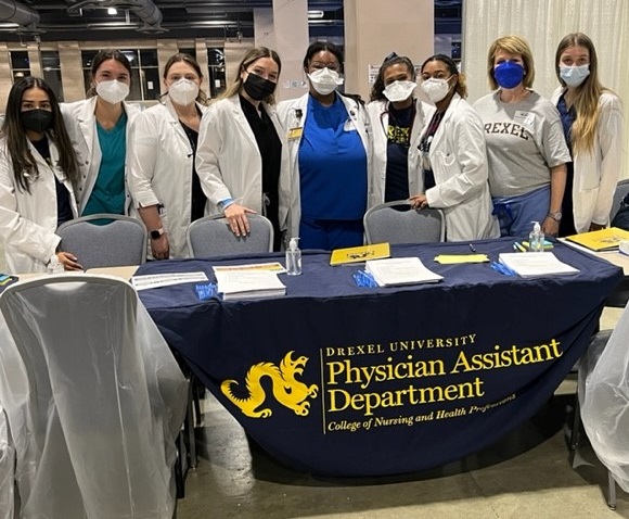 Group of people wearing white doctor's coats and masks standing behind a table with a banner stating Drexel University Physician Assistant Department